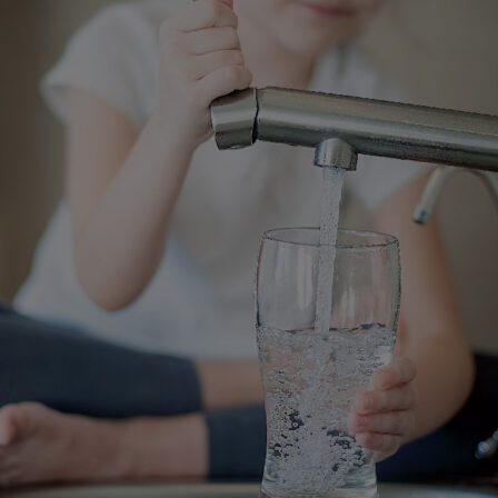 A child pours clean water from the faucet into a clear glass cup