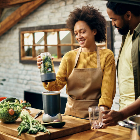 Happy African American couple using blender while preparing healthy smoothie in the kitchen.